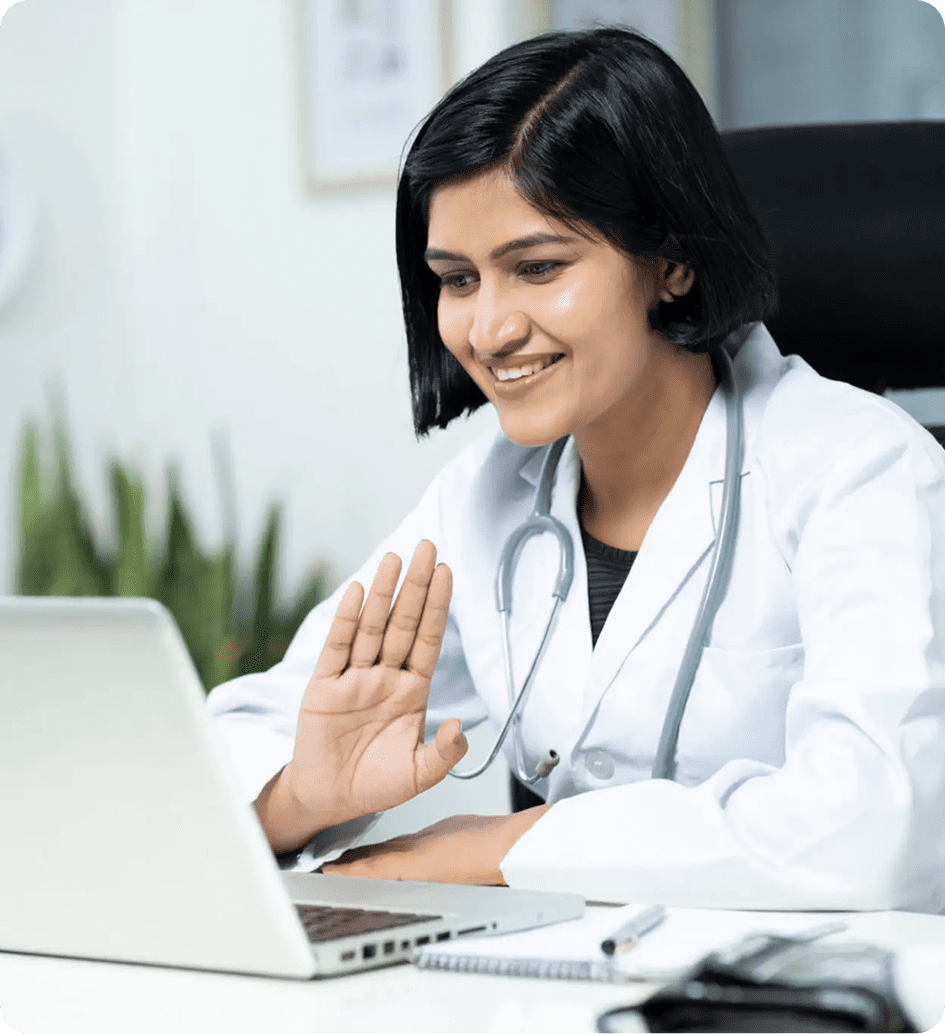 Female doctor smiling and waving during a video call on laptop.