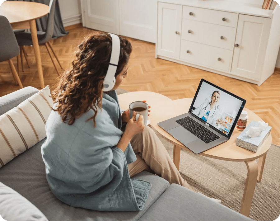 Woman video calling on laptop while sitting on couch with headphones.