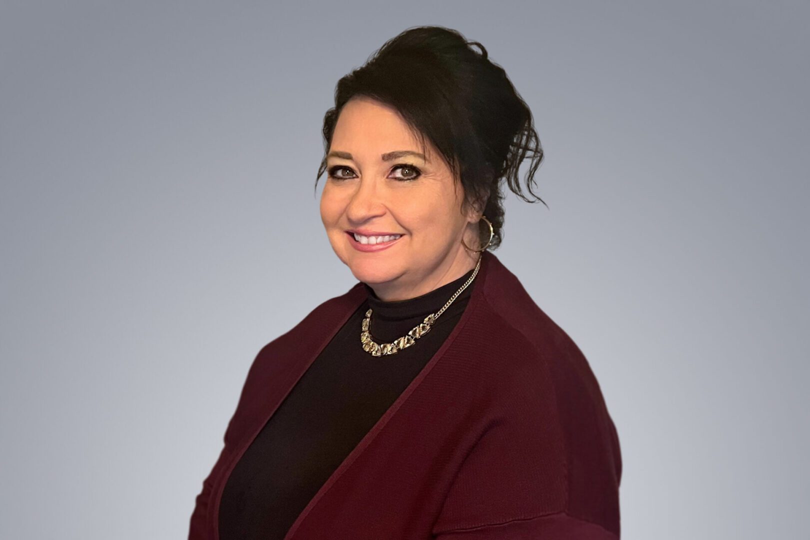 Professional woman smiling in business attire against a gray backdrop.
